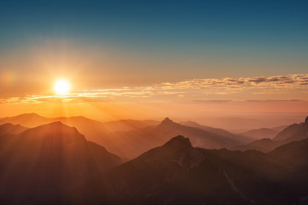 Hero Image: Radiant Sunrise/Sunset over the top of a mountain range. Yellow, orange, and red hues. Top 3rd is a dark blue sky.